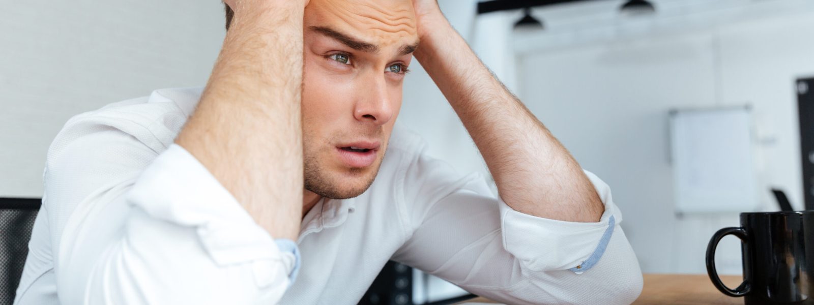 Upset disappointed young businessman sitting with hands on head